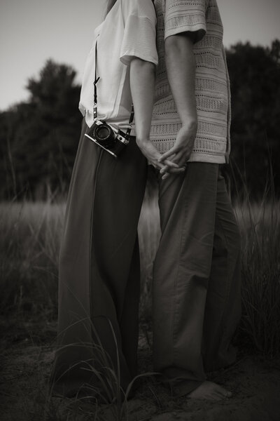 Black and white photo of Stephen and Kaity from Rainstorm Photo & Video standing together in tall grass, captured with a calm, cinematic tone that reflects their connection and artistry.
