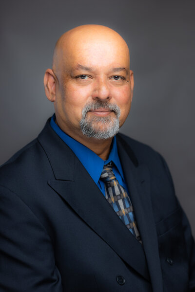 In-Studio headshot by Sacramento photographer of man in business suit and tie. He is slightly turned to his left and looking directly into camera.  He is partially smiling and looks confident and approachable.