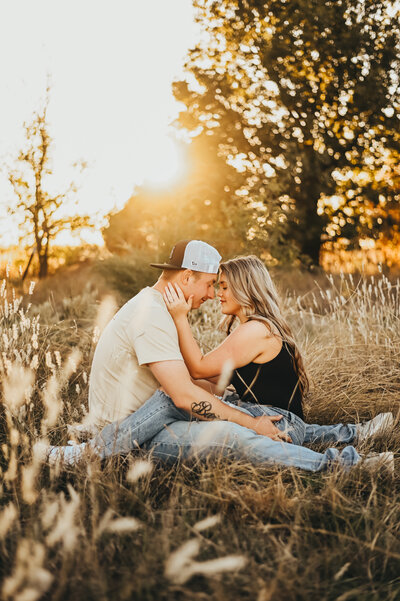 Couple cozied up together in a field during a golden hour engagement session 