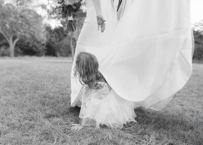 Black and white image of flower girl underneath the train of bride's dress