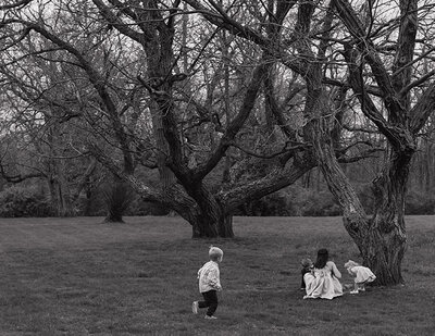 A black-and-white photo of four children playing near large, leafless trees in a grassy field ih Ohio. One child runs while others sit, evoking a peaceful, nostalgic mood.