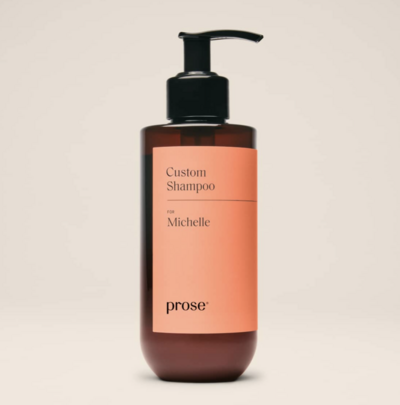 A personalized bottle of Prose custom shampoo with a black pump and sleek amber and blush-toned label. The label reads “Custom Shampoo” with a personalized name, highlighting its tailored haircare formulation.