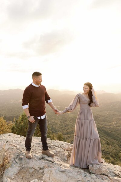 Couple walks holding hands on cliffside in Prescott for engagement photos