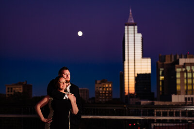 Couple standing in front of downtown Raleigh skyline with a full moon