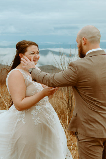groom wiping tear off of bride's cheek during elopement ceremony on mountaintop