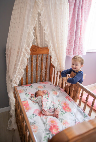 Brother starting down at newborn sister in crib | Taken by Maine Photographer who photographs in places like Sugarloaf, Maine