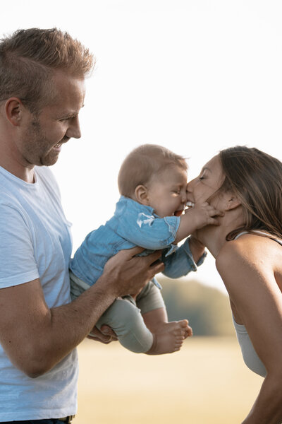 Dieser Schnappschuss zeigt ein Baby, dass sein Gesicht an das seiner Mutter hält und lacht, während der Vater es hält.