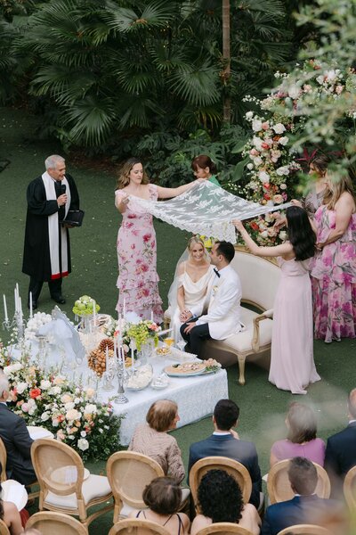A couple that just got married at an altar surrounded by colorful flowers, the groom is behind the bride, and in the background its the Château Bouffémont