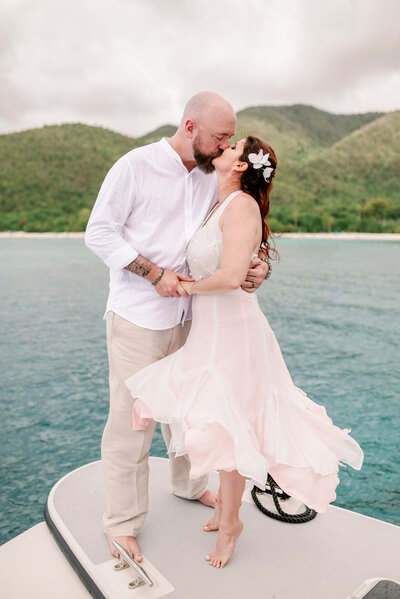 bride and groom kissing on the bow of a boat in the virgin islands. She is on her tippy toes while he leans down to meet her lips