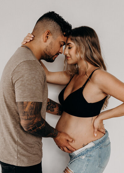 tattooed dad holds pregnant wife's belly during a studio session in parker colorado