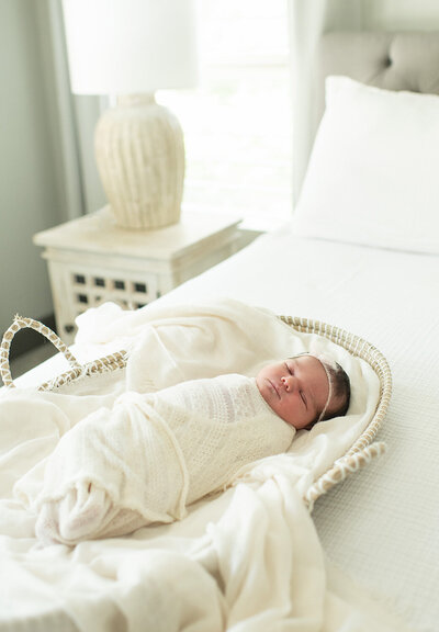 Newborn baby sleeps peacefully, swaddled in a white blanket on a cozy bed. A serene newborn session by Moments in Light Photography.