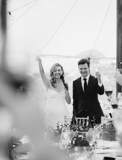 Bride and groom candidly raise glasses in cheers to their guests at their wedding reception. 
