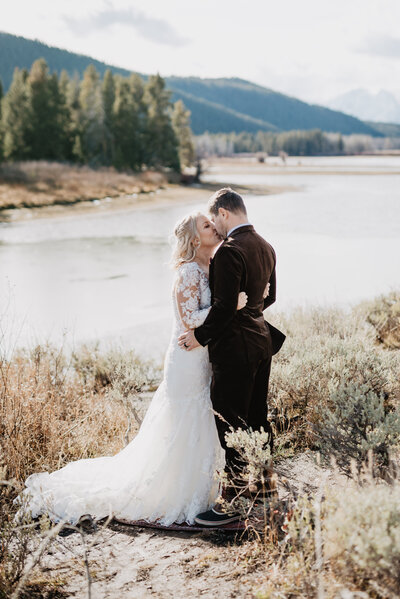 jackson hole wedding at oxbow bend in the winter with bride adn groom sharing their first kiss as husband and wife on the bank of the  frozen river
