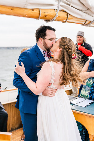 A couple kiss on a sailboat during their Portland, Maine wedding.