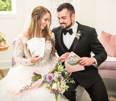 Bride and groom looking at feminine pink wedding invitations featuring a watercolor painting of White Fox Cottage in the envelope liner, delighted with their beautiful creation