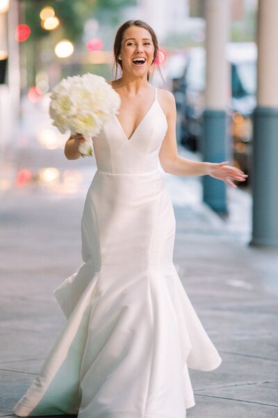 Stunning bride runs down a sidewalk holding her bouquet in her wedding dress