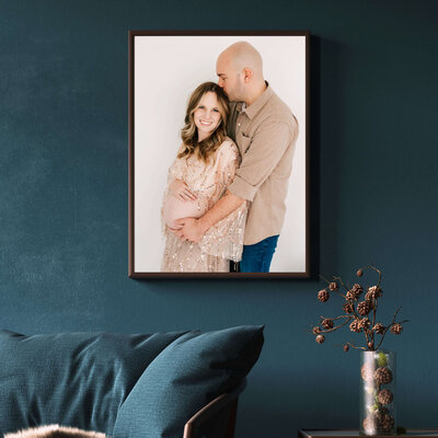 framed photo of pregnant couple cuddling on blue wall over couch captured by Joplin MO maternity photographer