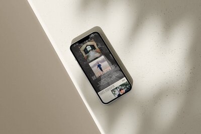A smartphone displaying a promotional flyer for small business website design services with text and images lies on a light-colored, textured surface with shadows.