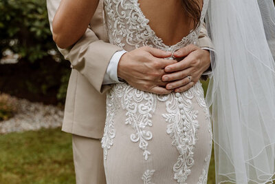 Close-up of a groom holding the bride's waist, showing intricate lace detail