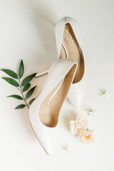 Detail shot of white high heels on a white mat styled with little light pink flowers.