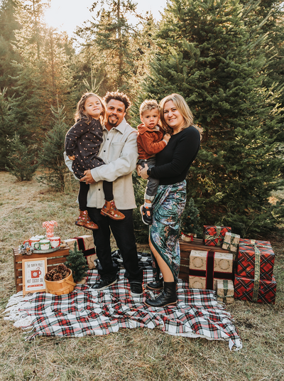 family portrait of a mom a dad a son and a daughter on a christmas tree farm with presents and cocoa