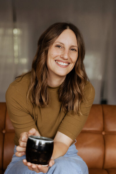 A person sitting on a couch smiling while holding a cup of coffee 