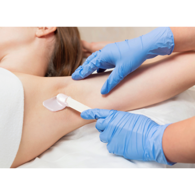 An esthetician wearing gloves applies hard wax to a client's underarm