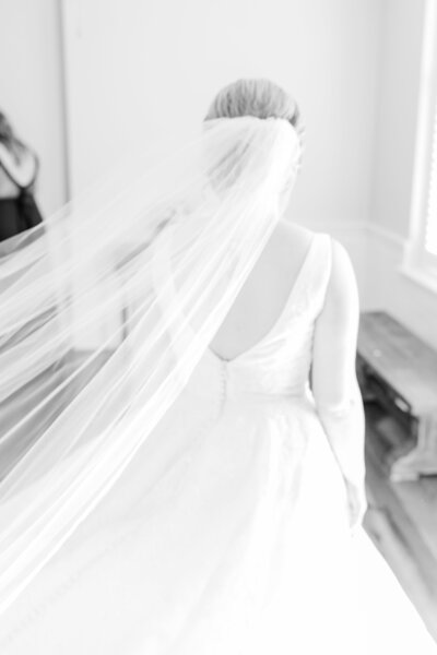 A dreamy black-and-white shot of a bride walking indoors, her long veil floating behind her in soft motion