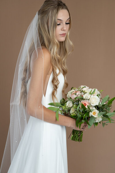Bride wearing a waltz length veil with pearls and serged edge and holding a white and blush bouquet