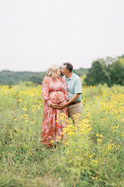 Expecting parents kiss in field of yellow flowers during Summer maternity photo session outdoors