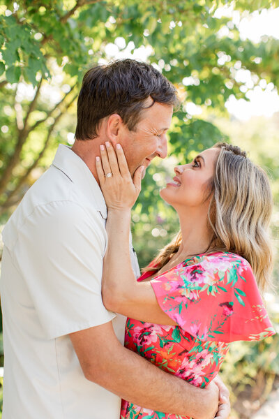 Engagement photo in Boone, NC of a couple smiling at each other and standing with the blue ridge mountains in the background at sunset.