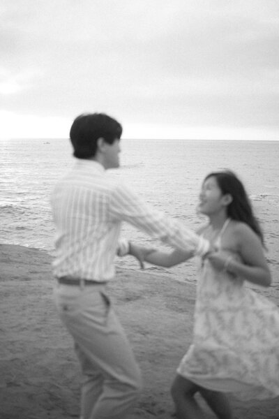 Blurry black-and-white photo of a playful couple laughing by the ocean, symbolizing emotional connection and relational healing through online couples therapy in Pasadena