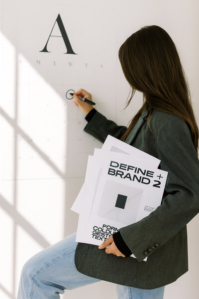 a brunette woman holding branding sheets circling a calendar
