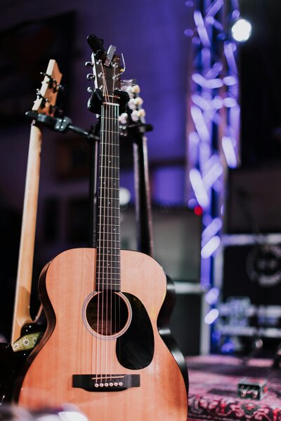 Photo of a light colored acoustic guitar on a stage under stage lights.
