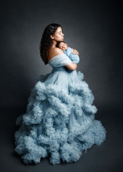 A beautiful moment of a mom holding her newborn baby. The mom is wearing a soft, flowing tulle dress, adding a touch of elegance.