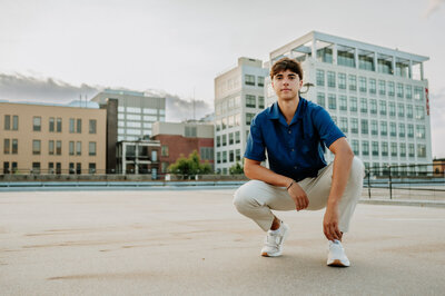 Boy crouching on the pavement with the city behind him.