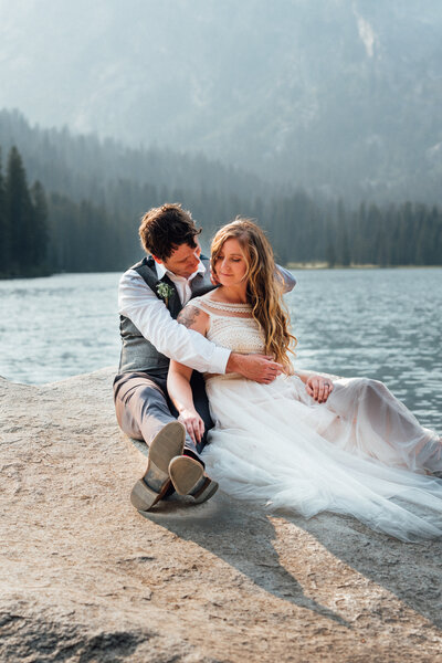 bride and groom sitting on lakeside