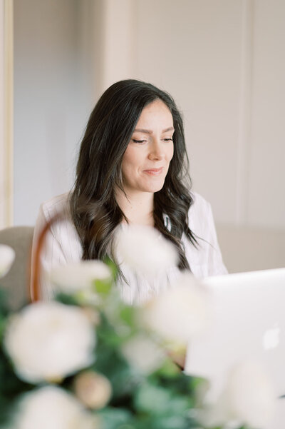 A corporate event planner and designer working on her laptop with a floral arrangement in the foreground