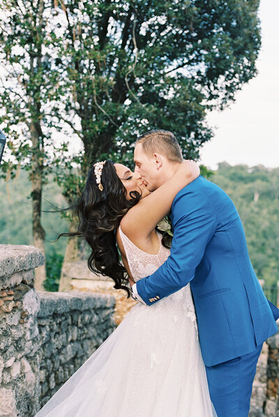 Bride and groom sharing a joyful kiss surrounded by lush greenery and stone architecture at Altos de Chavón — destination wedding captured by Asia Pimentel Photography.