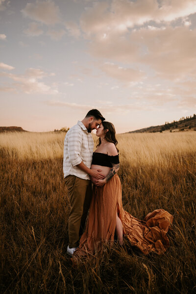 A pregnant mom and a loving dad touch her baby belly in Lory State Park in the fall