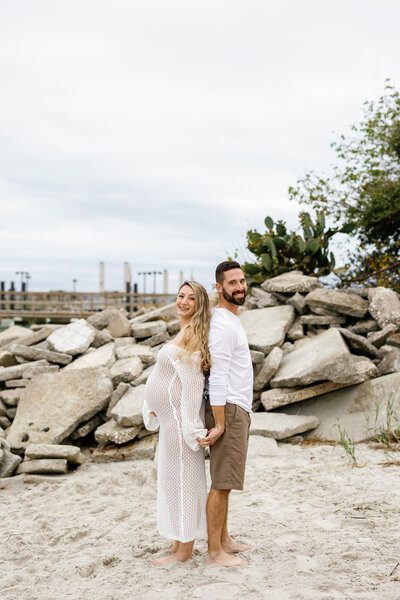 Expectant couple standing back-to-back on Wilmington beach, romantic sunset maternity photography