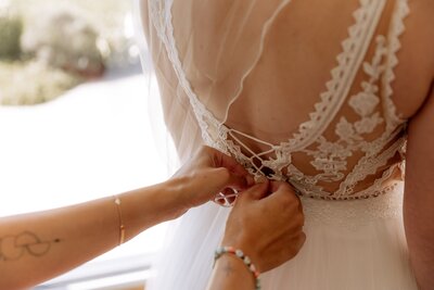 Detailfoto von dem Rücken einer Braut während das Hochzeitskleid zu gemacht wird