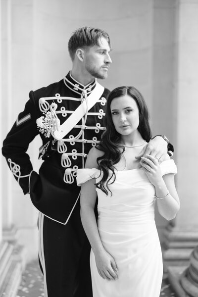 Bride and groom man wearing military uniform and bride wearing gown standing in front 