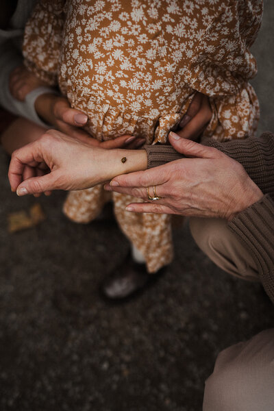 Close-up of family hands admiring a ladybug resting on a wrist, with a child in a mustard floral dress in the background — candid Orange County family photography detail shot.