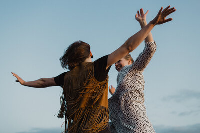 Aikuiset kaksi siskosta tanssii kädet levällään taivasta vasten Suomenlinnassa Helsingissä