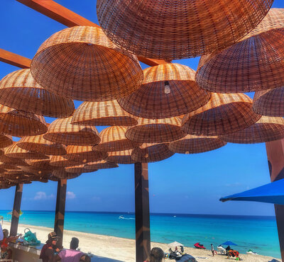 A shaded beachfront seating area with woven rattan umbrellas overlooking the ocean, ideal for honeymooners and destination wedding guests.
