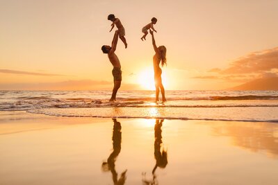 family of four tossing kids in to air and laughing at sunset in maui