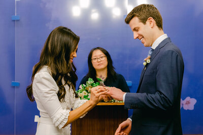 The bride places a ring on her  groom's finger during their wedding at NYC City Hall