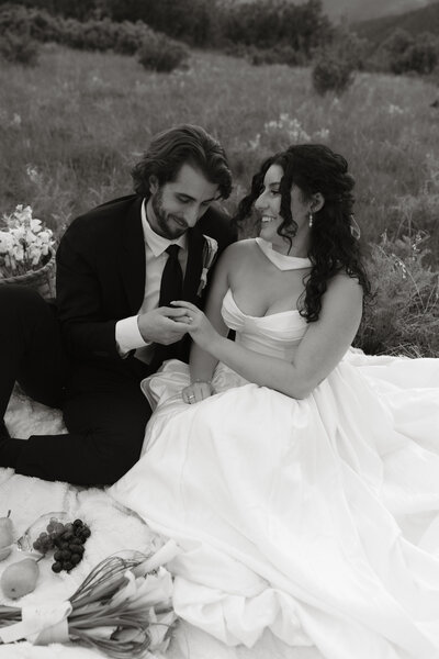 Black and white photo of a bride and groom sitting on a blanket after their wedding ceremony, sharing a quiet, joyful moment captured by Rainstorm Photo & Video in a romantic, documentary style.