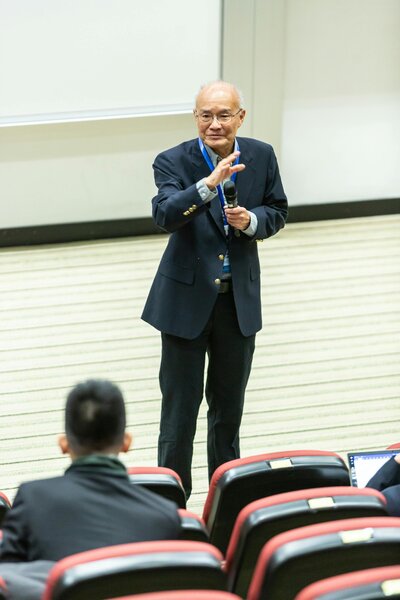 An older Asian man in a suit speaks to a class